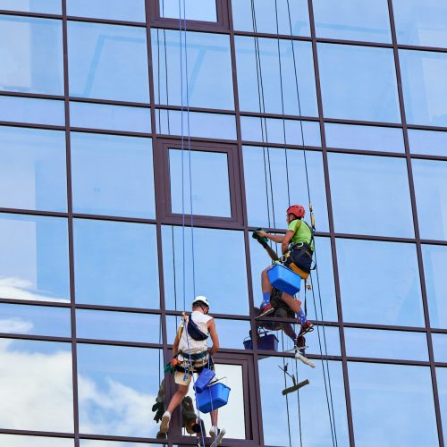 Industrial mountaineering worker cleaning window outside building.